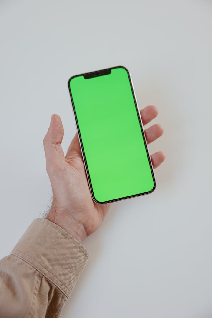 Close-up of a hand holding a smartphone with a green screen, ideal for mockup and design presentations.
